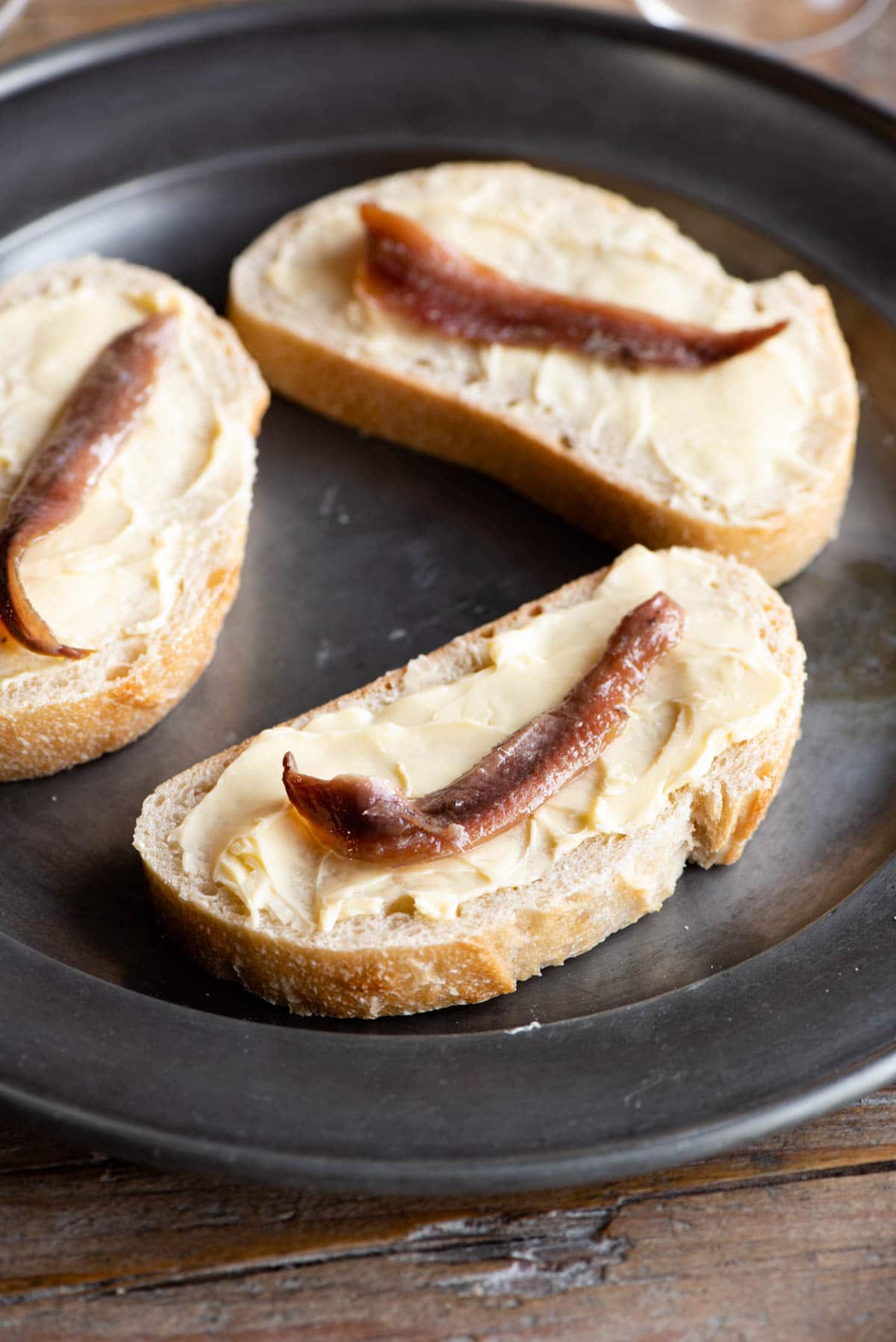 A close up of a slice of bread spread with butter and topped with an anchovy