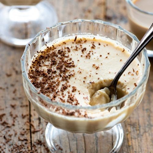 Baileys panna cotta in a small glass dish with a spoon and grated chocolate on top