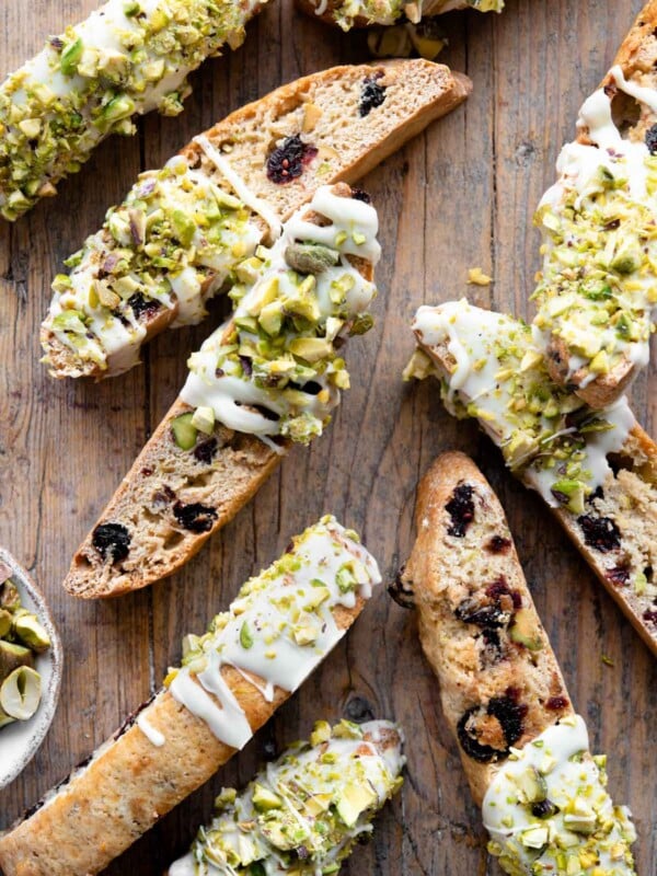 An overhead shot of cranberry and pistachio biscotti on a wooden background drizzled with white chocolate