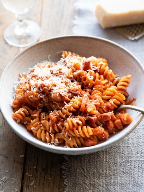 Creamy tomato pasta in a bowl sitting on a wooden surface with a glass of wine in the background