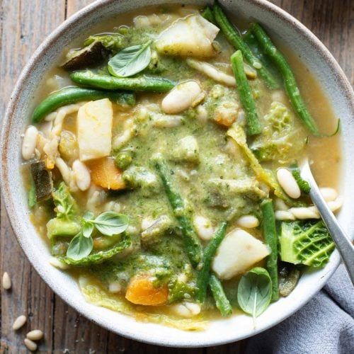 An overhead shot of a bowl of Ligurian minestrone with lots of vegetables and basil pesto sitting on a wooden background