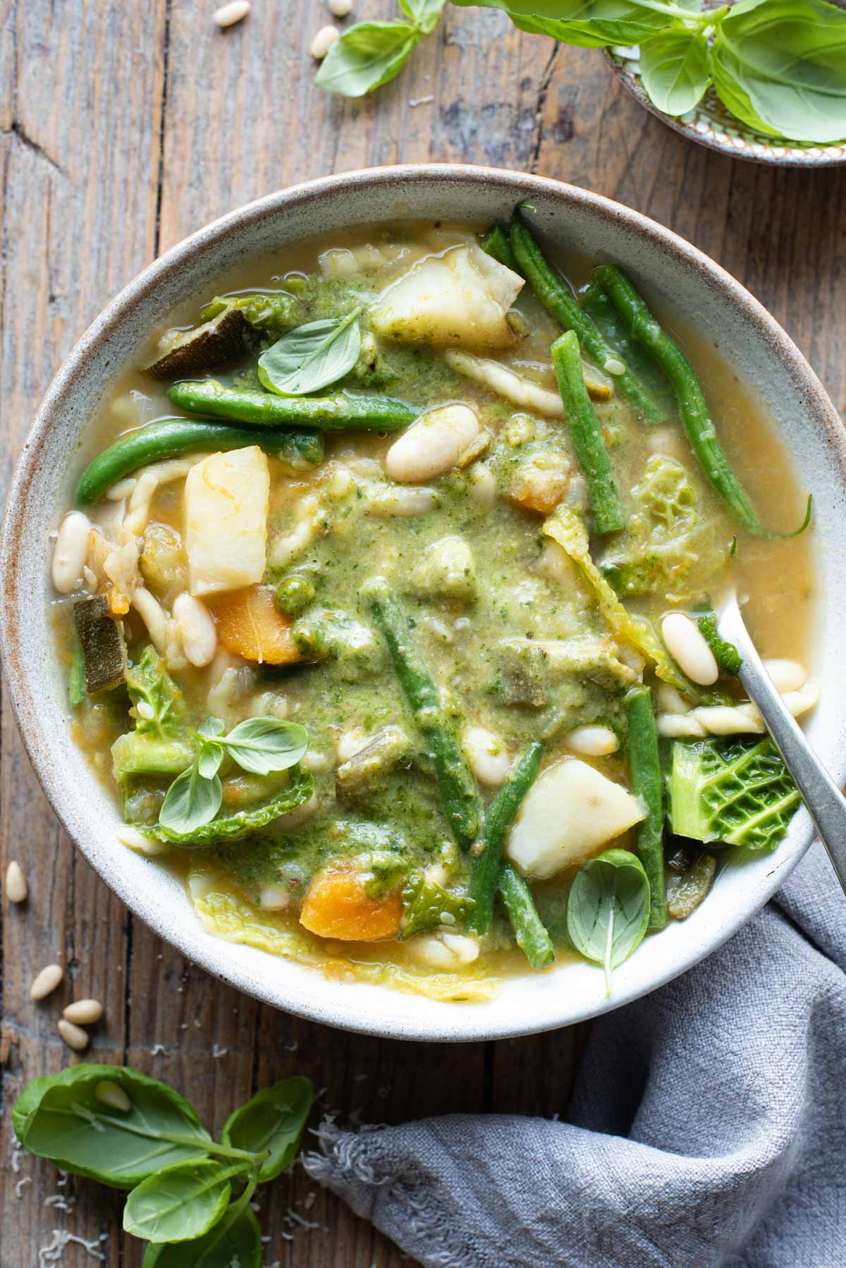 An overhead shot of a bowl of Ligurian minestrone with lots of vegetables and basil pesto sitting on a wooden background