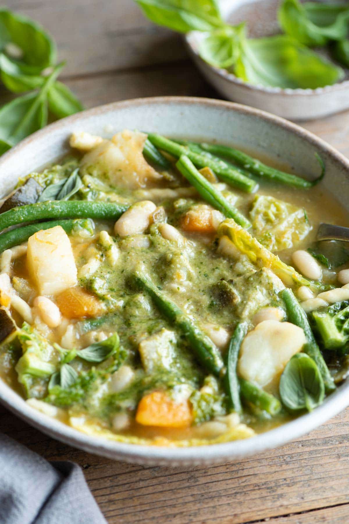 A close up of a bowl of minestrone soup with lots of mixed vegetables and basil pesto