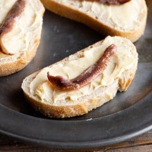 A close up of a slice of bread and butter topped with an anchovy