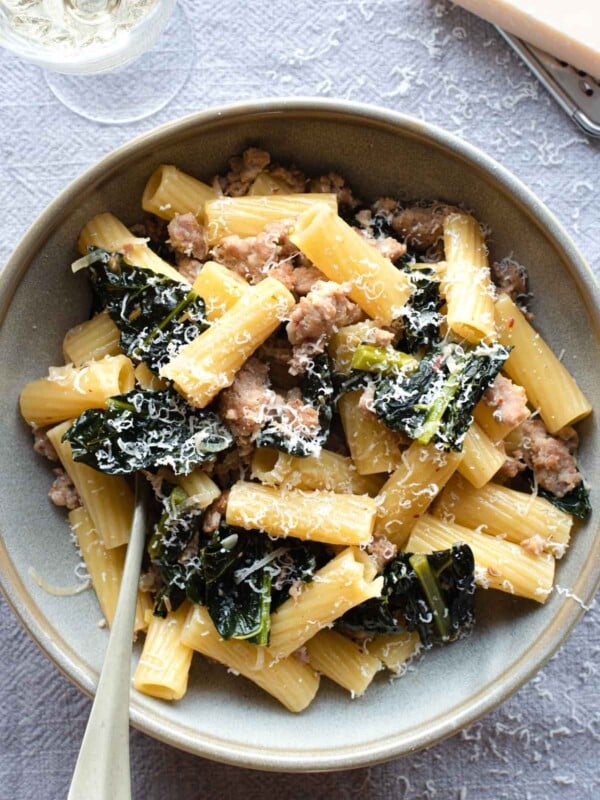 An overhead shot of a bowl of pasta with kale and sausage with a glass of wine at the side