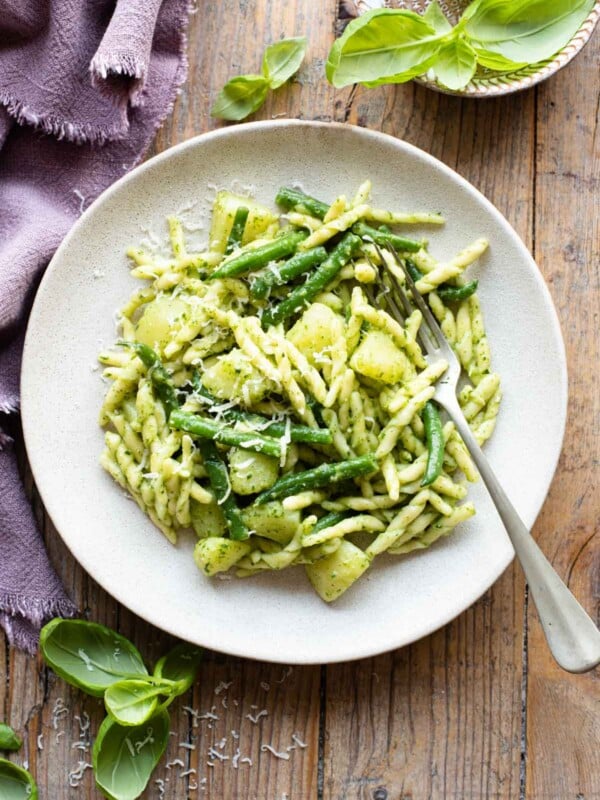 Trofie pasta with pesto, potatoes and green beans on a plate sitting on a wooden surface