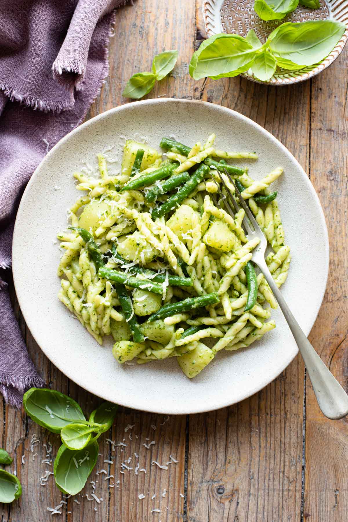 Trofie pasta with pesto, potatoes and green beans on a plate sitting on a wooden surface