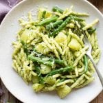 A close up of pesto pasta on a plate with potatoes and green beans