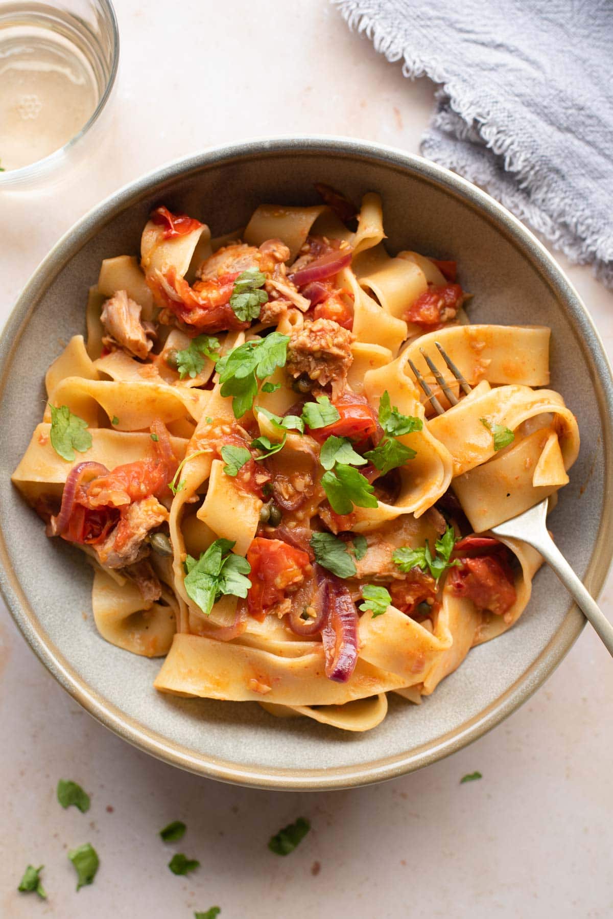 An overhead shot of tuna pasta in a bowl with tomatoes, capers and parsley