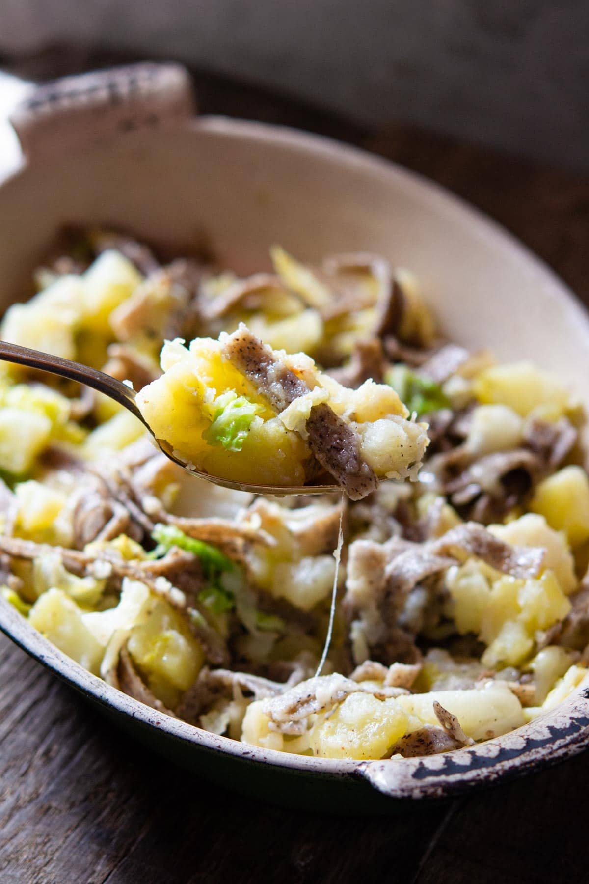 A close up of a spoonful of pizzoccheri pasta with potatoes, cabbage and cheese
