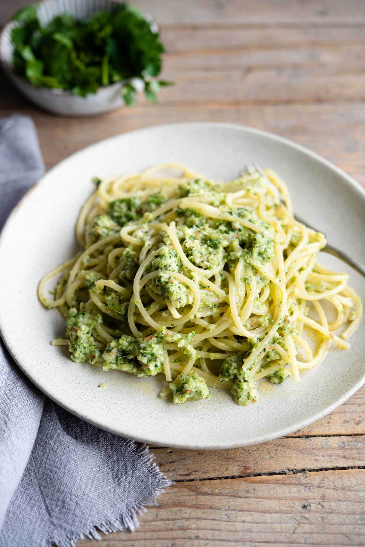 A plate for zucchini pesto pasta on a wooden surface with a blue towel at the side