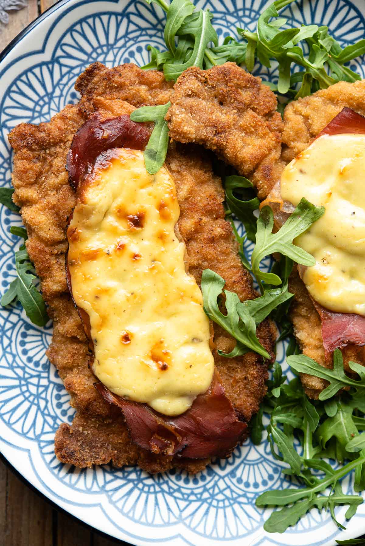 An overhead shot of breaded veal cutlets on a plate topped with parmesan cream and prosciutto