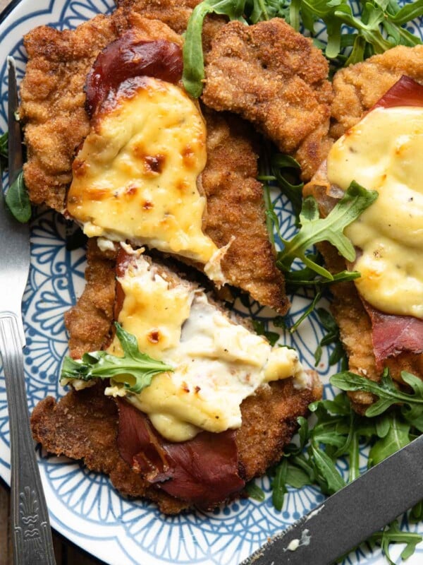 A close up of a veal cutlet cut in half with parmesan cream and prosciutto on top