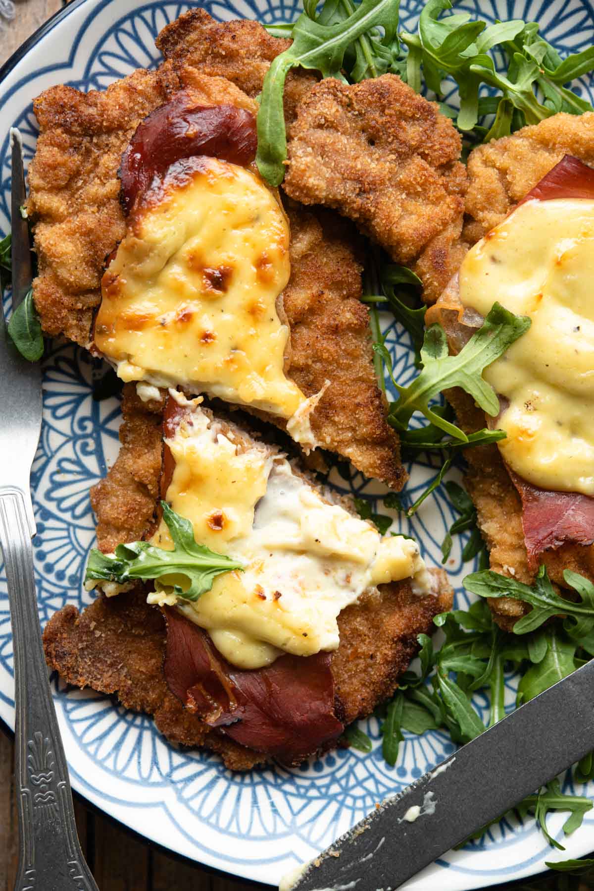 A close up of a veal cutlet cut in half with parmesan cream and prosciutto on top