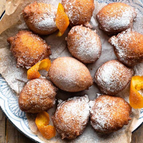 An overhead shot of small ricotta doughnuts on a plate dusted with powdered sugar