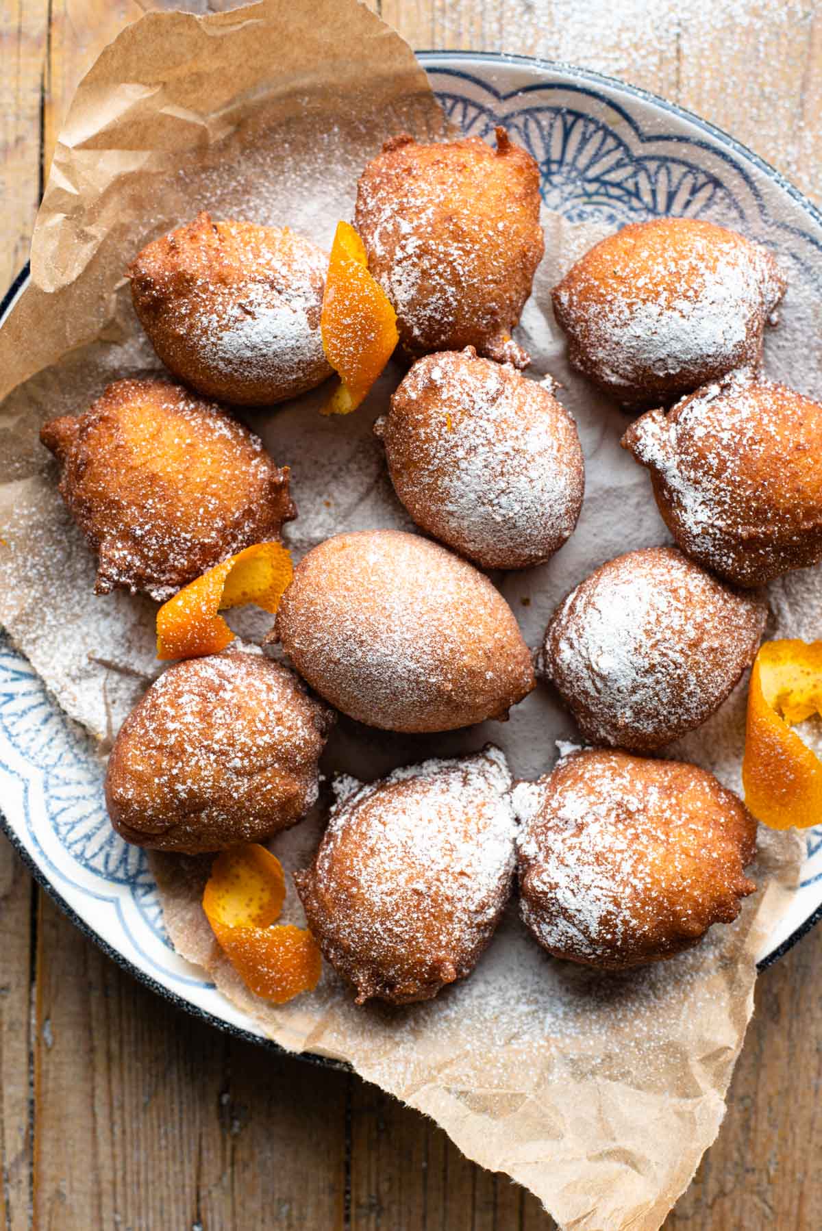 An overhead shot of ricotta doughnuts on a blue patterned plate dusted in powdered sugar.