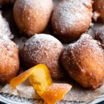 A close up of ricotta doughnuts on a plate with twisted orange peel at the side