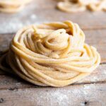 A close up of Tonnarelli pasta rolled into a nest sitting on a rustic wooden surface