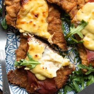 A close up of a veal cutlet cut in half topped with prosciutto and parmesan cream