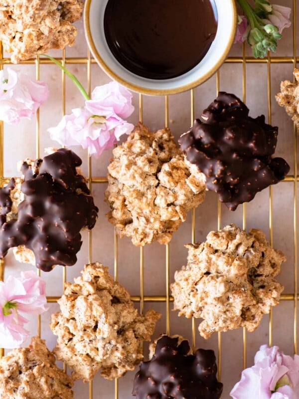 An overhead shot of both original and chocolate Brutti ma Buoni cookies on a gold cooling rack with pink flowers dotted around
