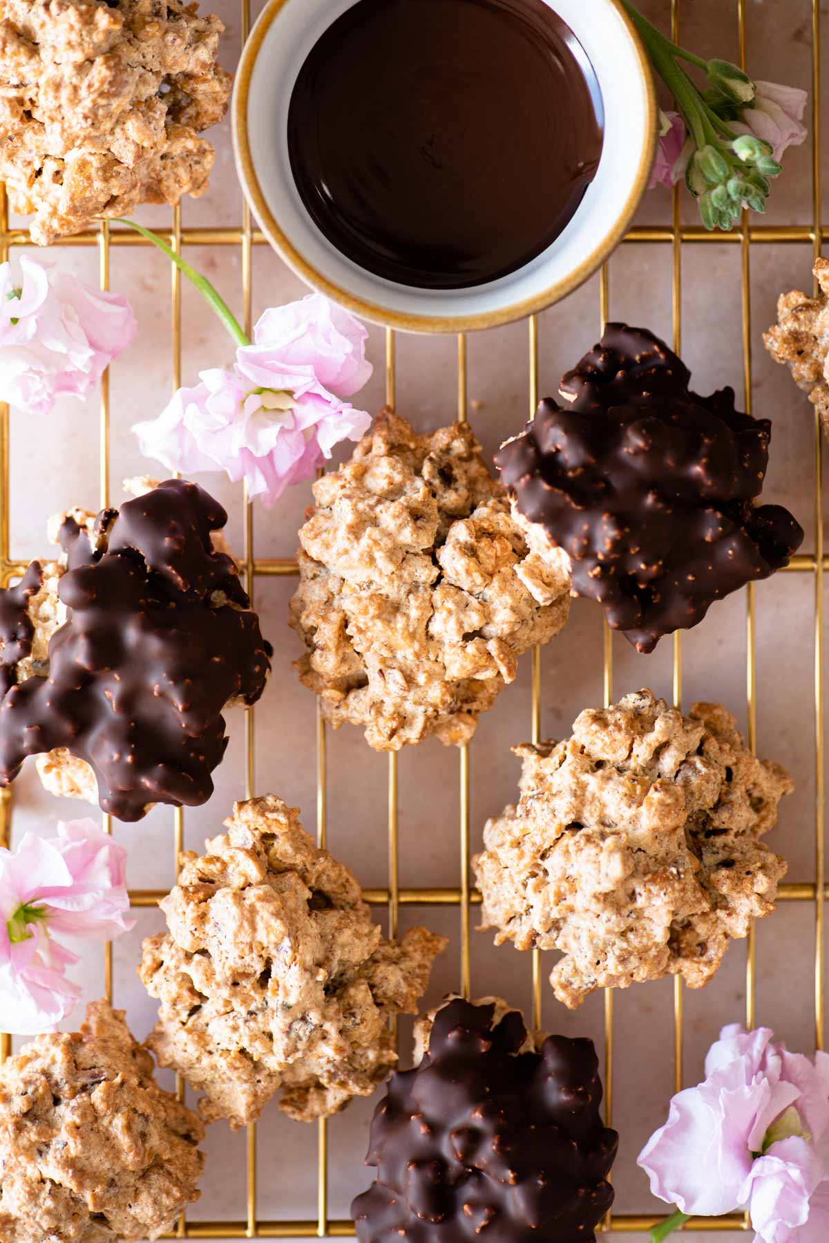 An overhead shot of both original and chocolate Brutti ma Buoni cookies on a gold cooling rack with pink flowers dotted around