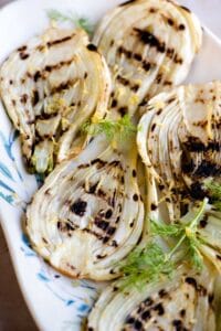 Slices of grilled fennel on a serving plate with lemon zest on top