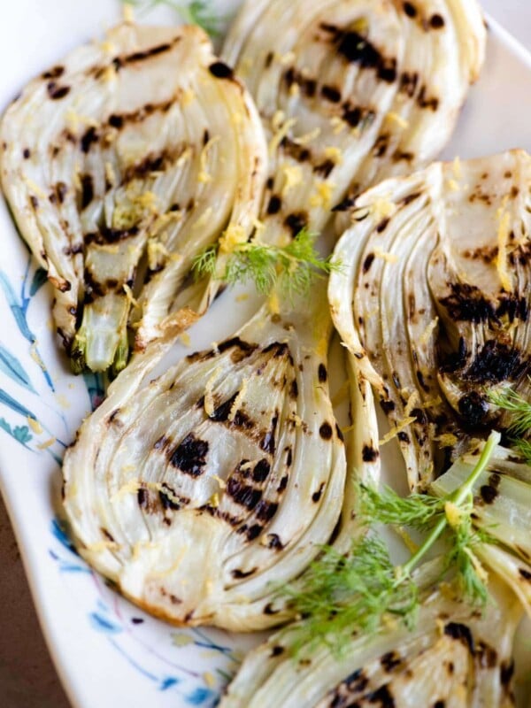 Slices of grilled fennel on a serving plate with lemon zest on top