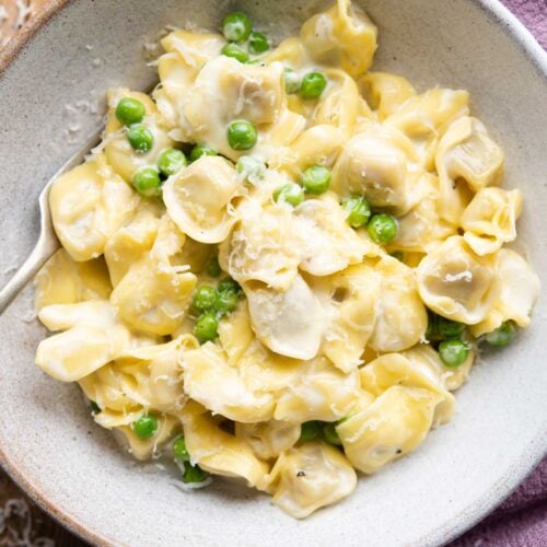 An overhead shot of Tortellini in a bowl with a cream sauce and peas