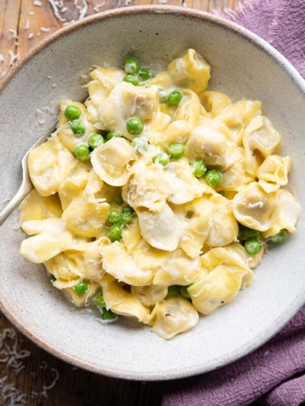 An overhead shot of Tortellini in a bowl with a cream sauce and peas
