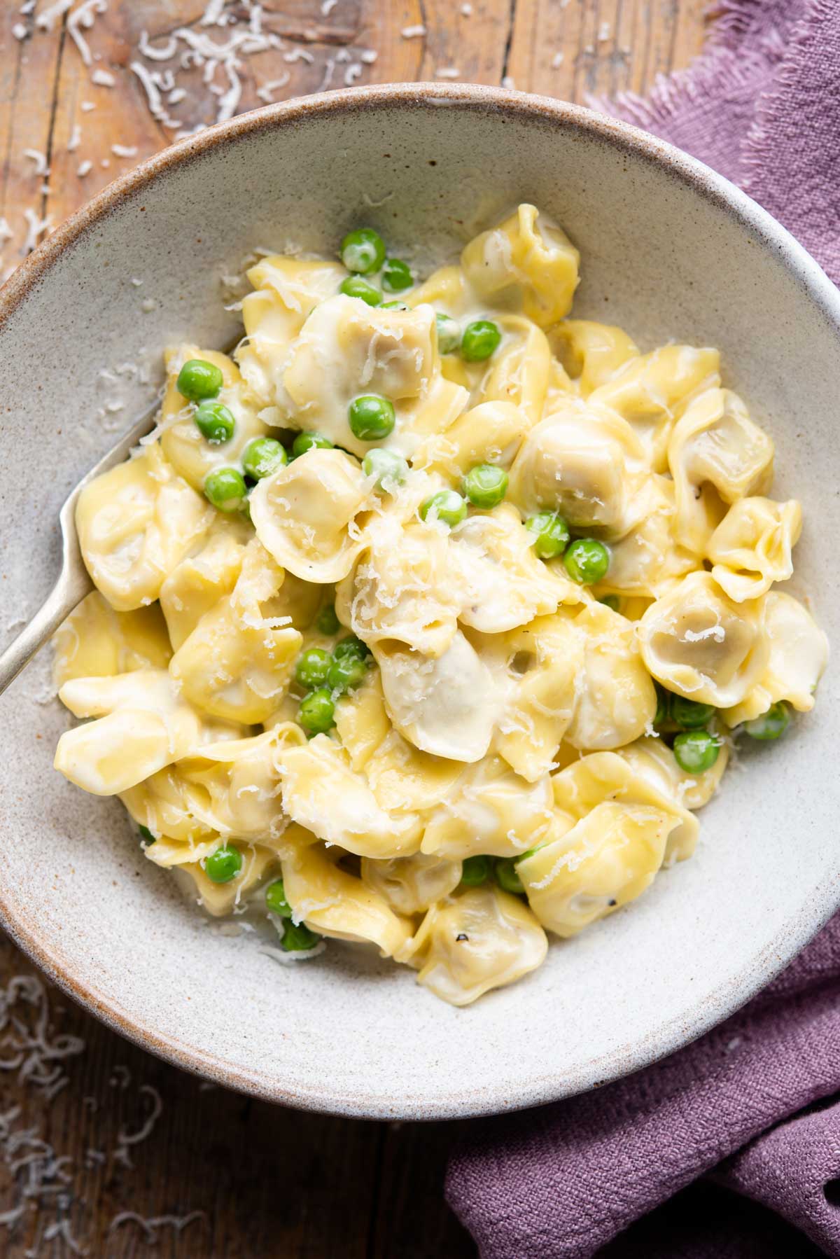 An overhead shot of Tortellini in a bowl with a cream sauce and peas