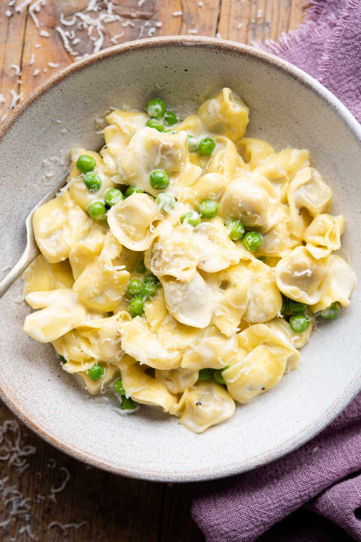 An overhead shot of tortellini pasta in a bowl with a creamy sauce and peas.