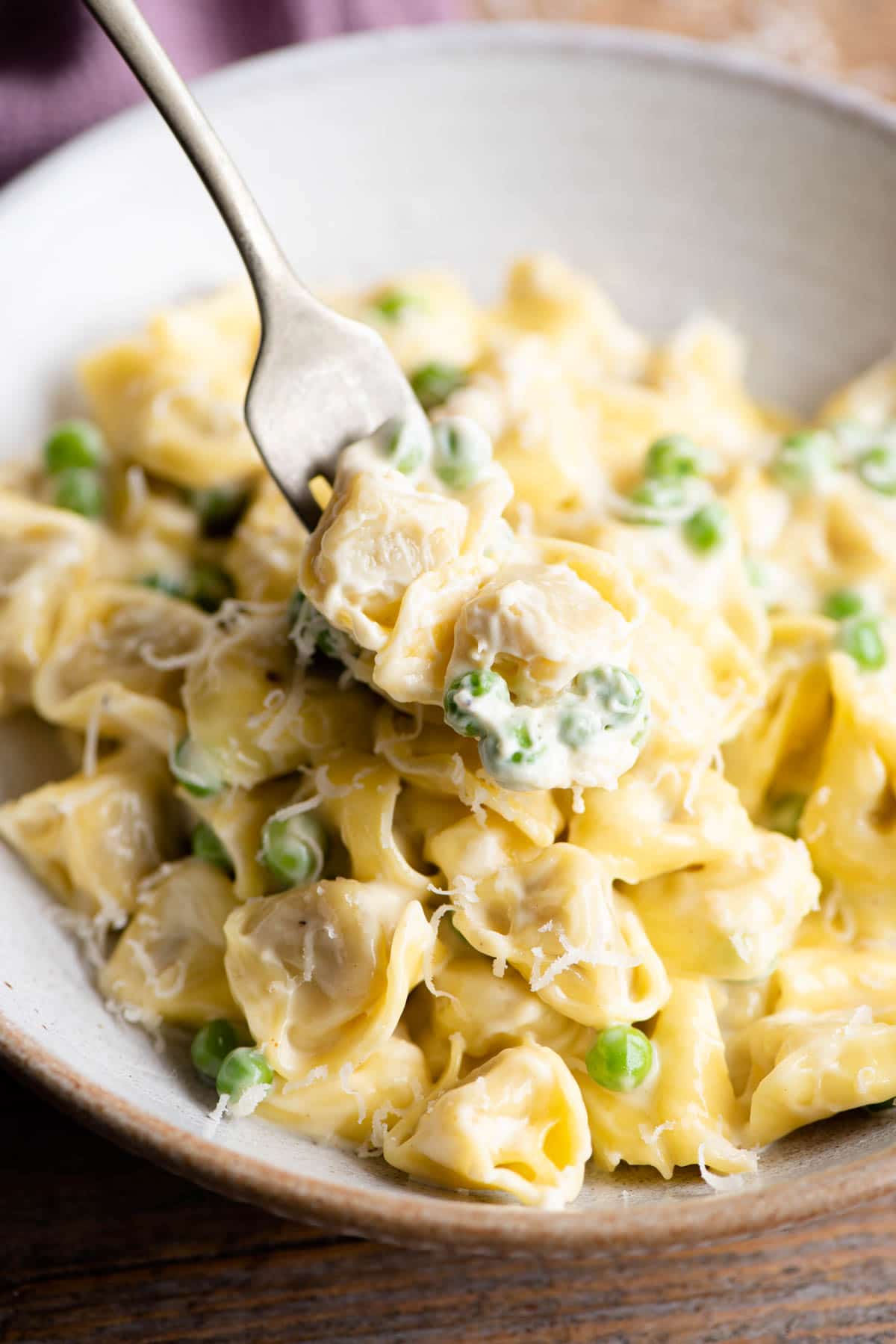 A close up of two Tortellini on a fork with cream and peas