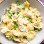 A close up of Tortellini alla Panna in a bowl with peas
