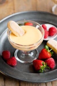 A small glass bowl filled with Zabaglione and a savoiardi cookie dunked into it