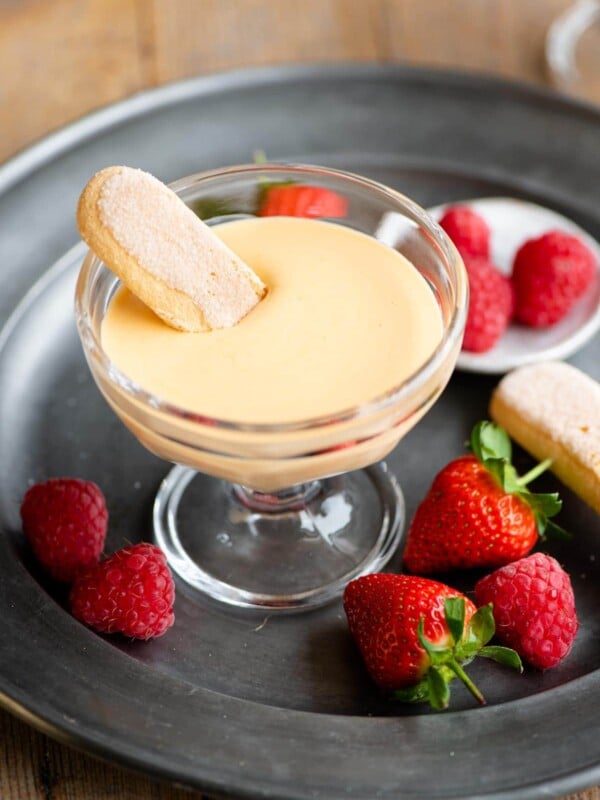 A small glass bowl filled with Zabaglione and a savoiardi cookie dunked into it