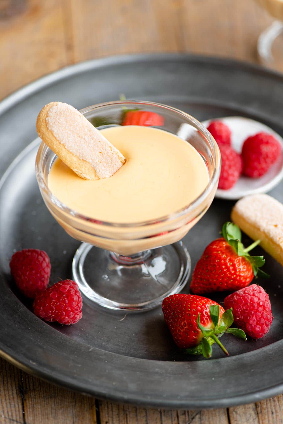 Zabaglione in a small glass dish with a ladyfinger dunked inside and berries at the side