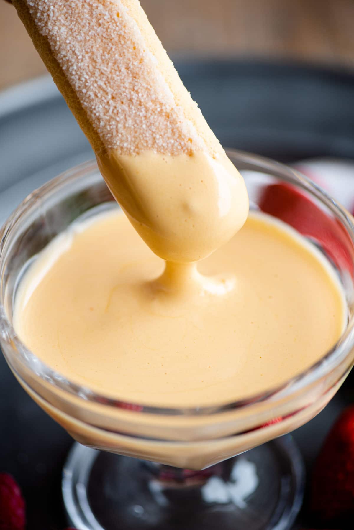A close up of a savoiardi cookie being dunked into zabaglione