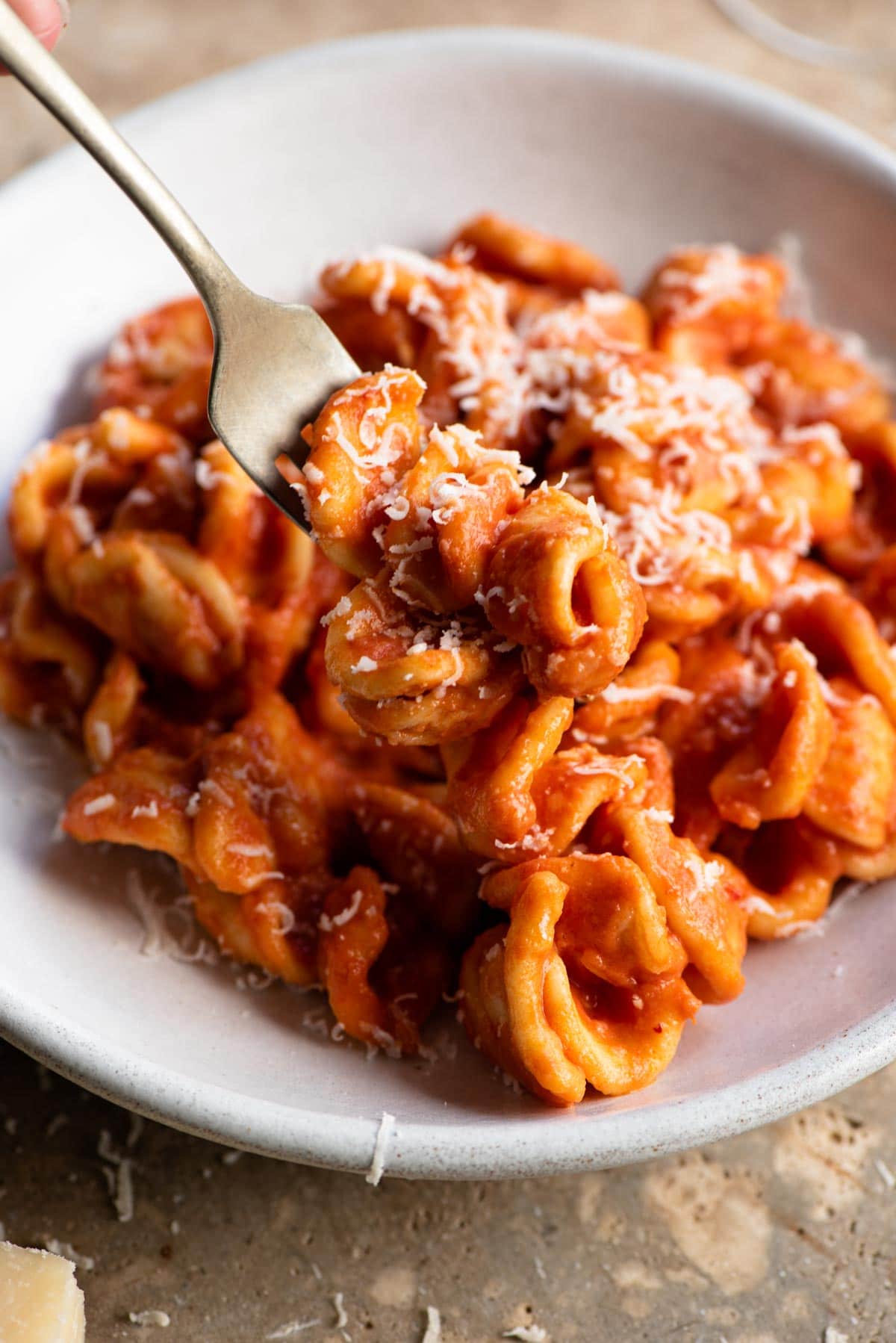 A close up of a fork picking up some orecchiette with a cream tomato Nduja sauce from a bowl