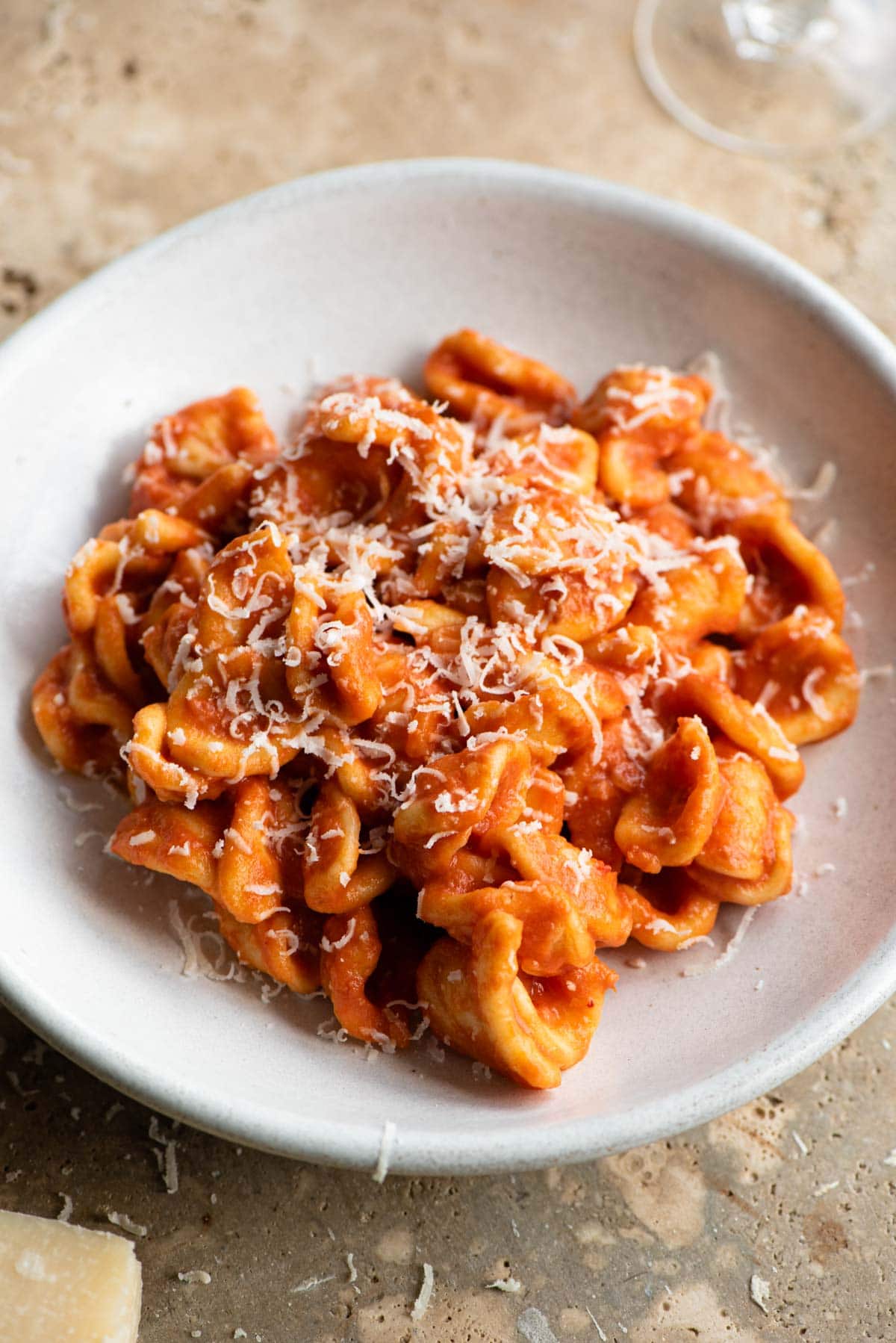 Orecchiette pasta with a creamy tomato sauce in a rustic ceramic bowl topped with cheese