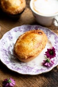 An Italian pastry called Pasticciotto on a small pink and white plate with pink flowers at the side.