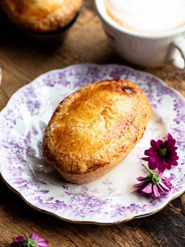 An Italian pastry called Pasticciotto on a small pink and white plate with pink flowers at the side.