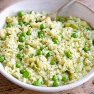 A side shot of a pea and pesto risotto in a bowl in a wooden surface with a fork at the side