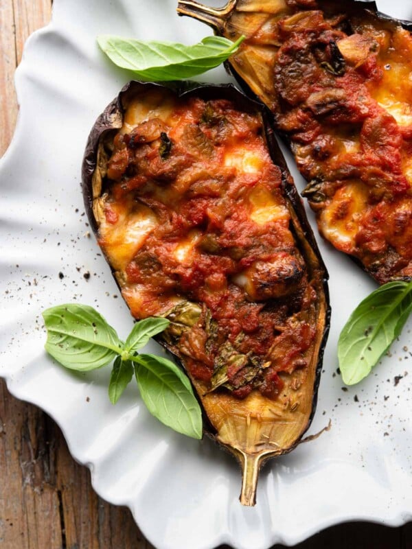 Two stuffed eggplants on a scalloped edged plate with basil scattered around.