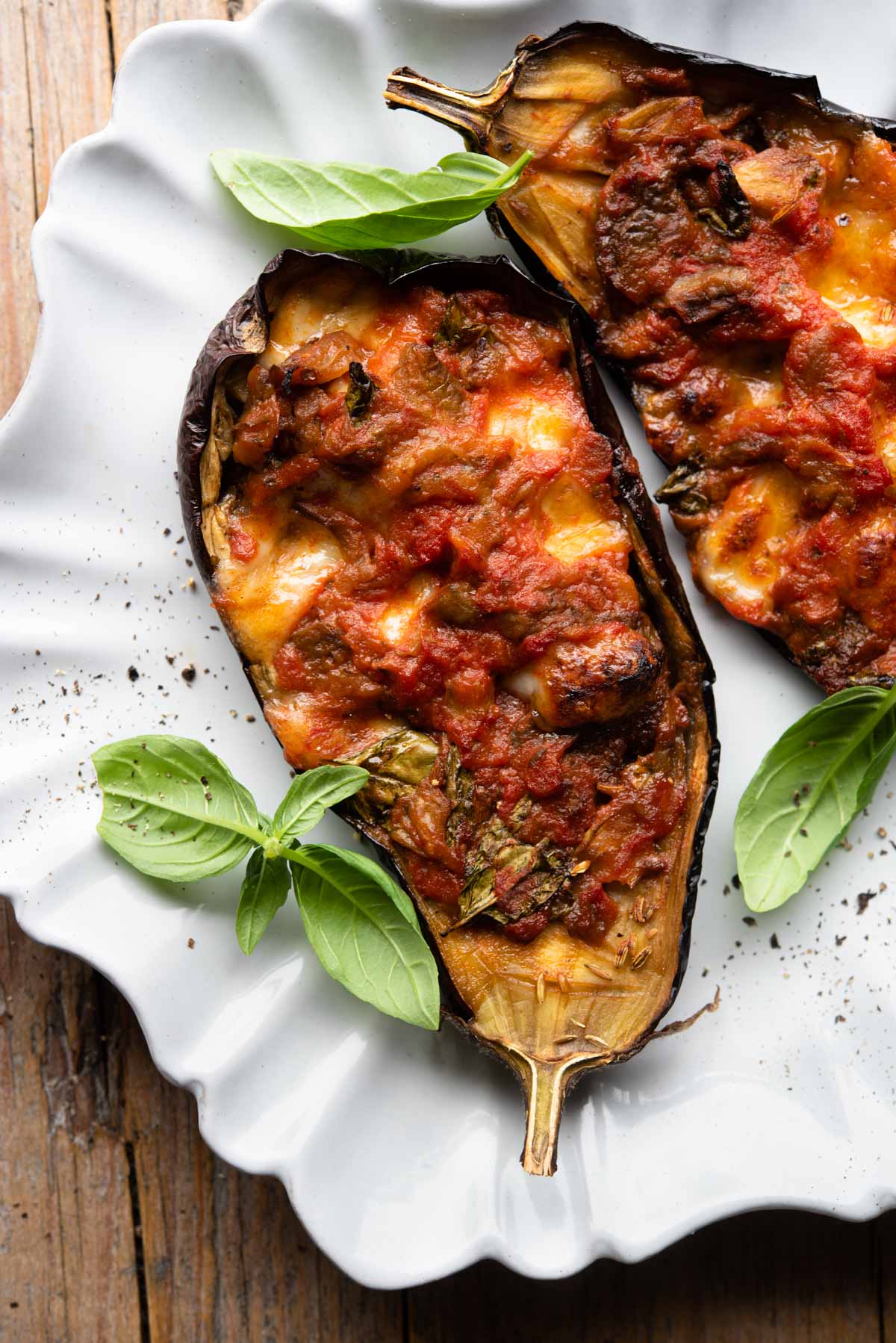 Two stuffed eggplants on a scalloped edged plate with basil scattered around.