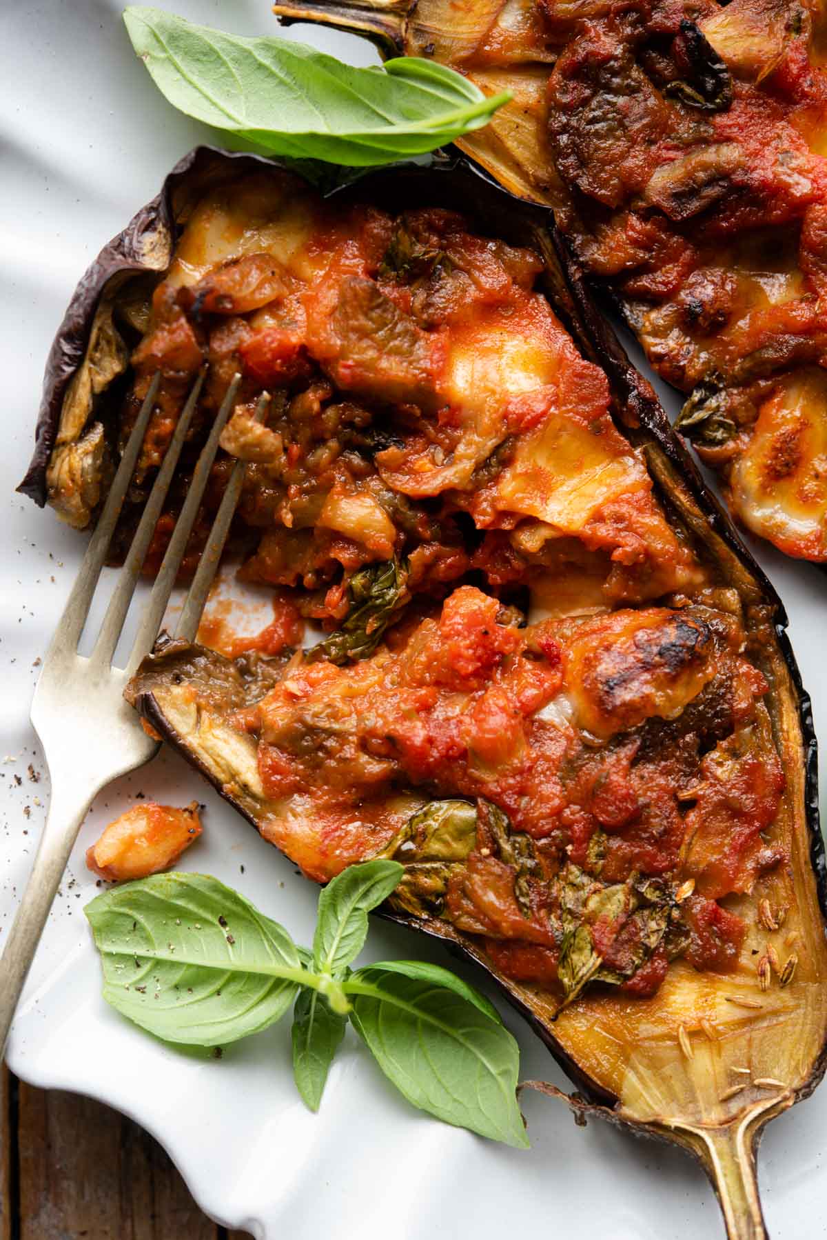 A close up of half an eggplant stuffed with tomato and mozzarella cut open on a plate.