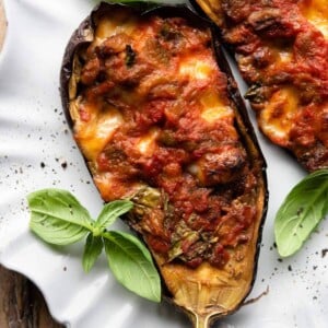 A close up of half a stuffed eggplant on a plate topped with fresh basil.