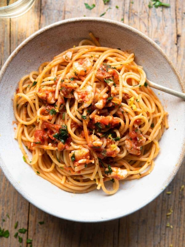 An overhead shot of shrimp spaghetti in a rustic bowl sitting on a wooden surface with a glass of white wine at the side.
