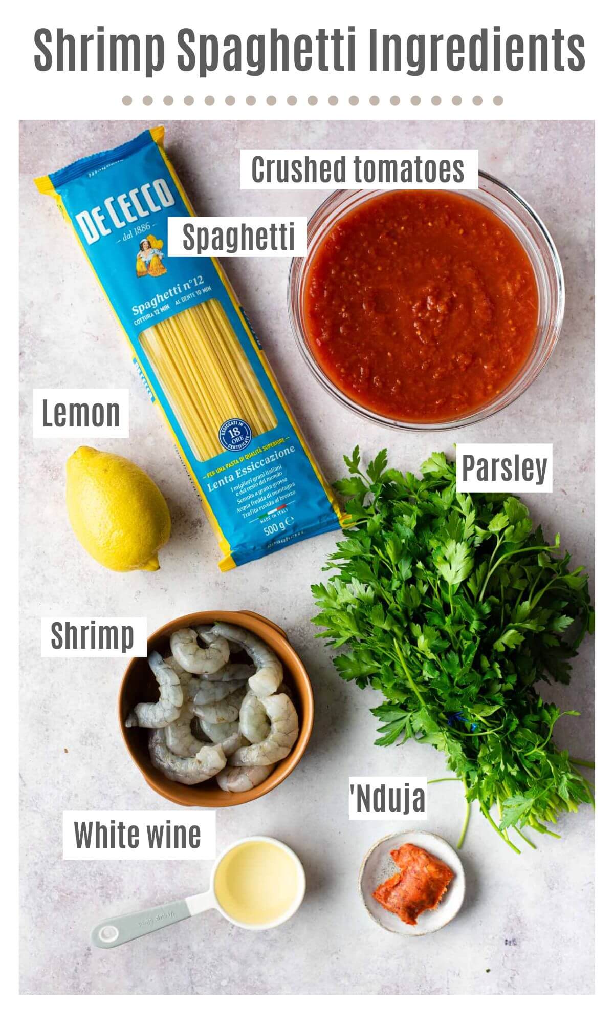 An overhead shot of ingredients needed to make shrimp spaghetti labelled; spaghetti, crushed tomatoes, lemon, parsley, shrimp, Nduja and white wine. 