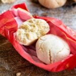 A close up of two amaretti cookies in a pink wrapper on a wooden surface.