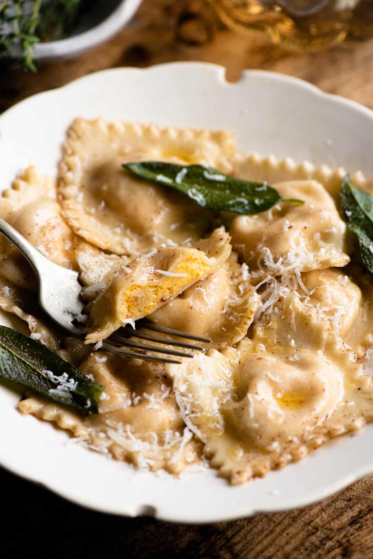 A close up of butternut squash ravioli and sage butter in a bowl with one ravioli cut in half showing the orange filling.